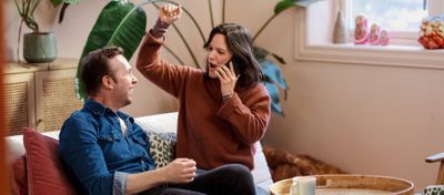 Foto av en mann og en kvinne som sitter i en sofa. Hun snakker i en telefon og jubler – han smiler og ser på henne. 