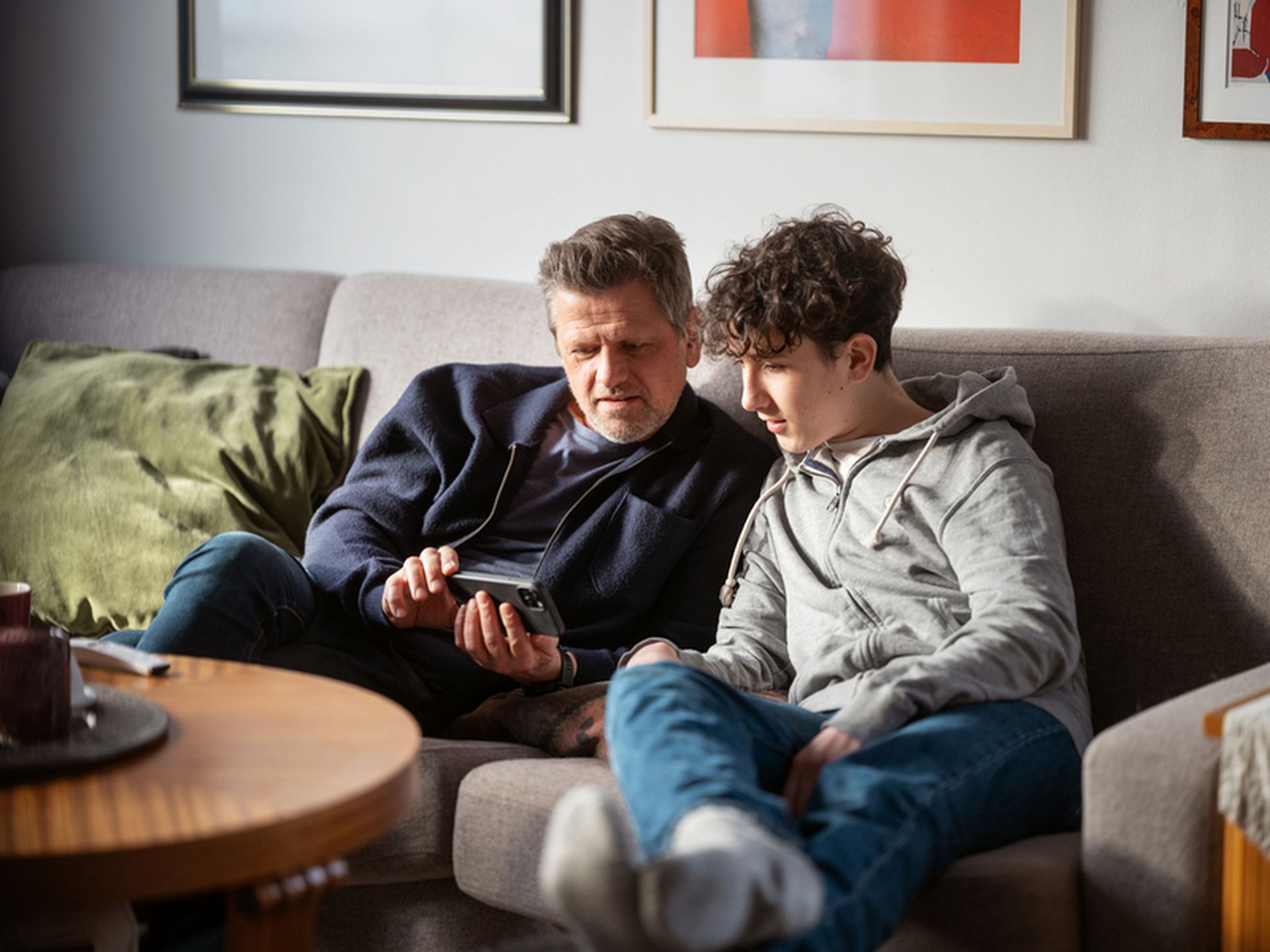 Far og sønn ser på mobil sammen i sofaen