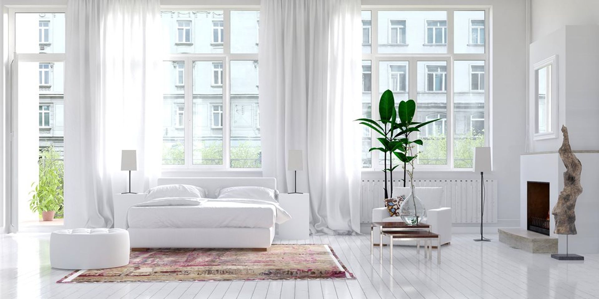 Hvitmalt stue med hvite møbler. Store vindu, hvite gardiner, planter og fargerikt gulvteppe. Bilde.