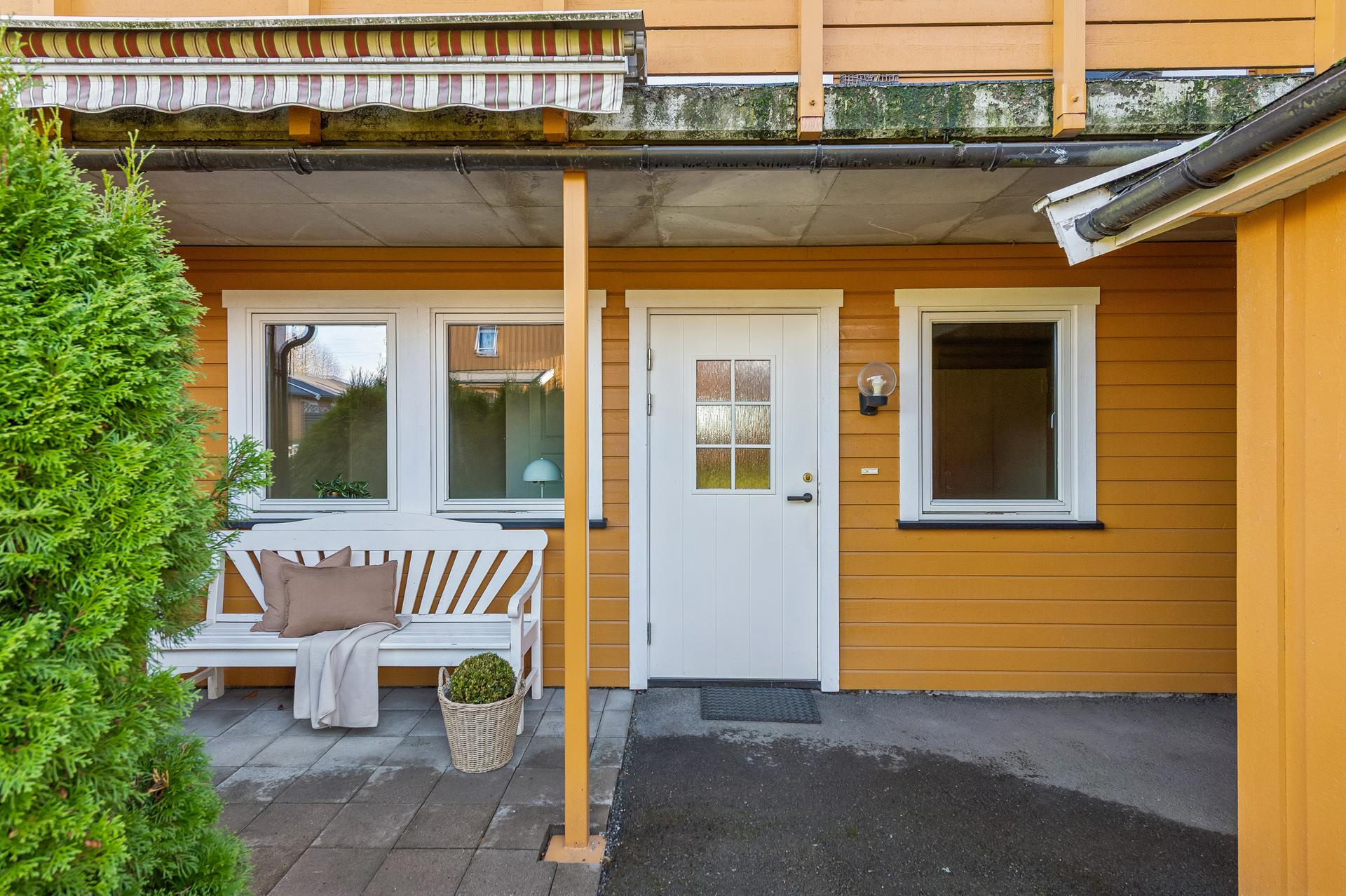 Overbygd inngangsparti mot vest med hellelagt markterrasse og sitteplass.. Bilde nummer 3 av 3