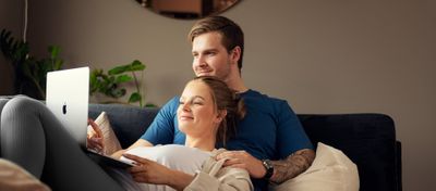 Ungt par i sofa ser på en mac-skjerm sammen. Foto