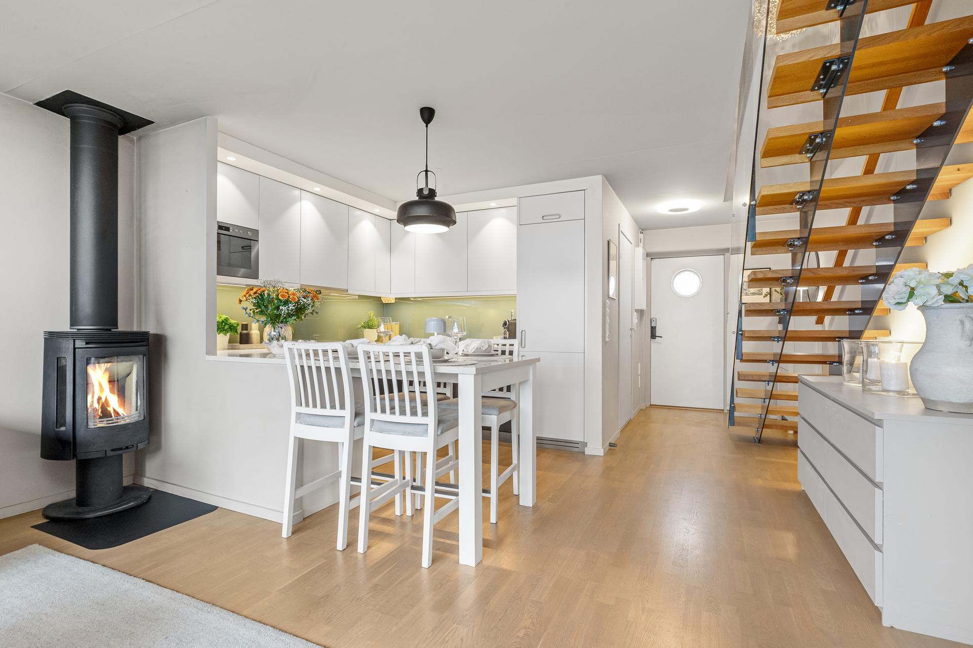 Kjøkkenet ligger i åpen løsning mot stuen med integrert spiseplass og peisovn.. Bilde nummer 3 av 3