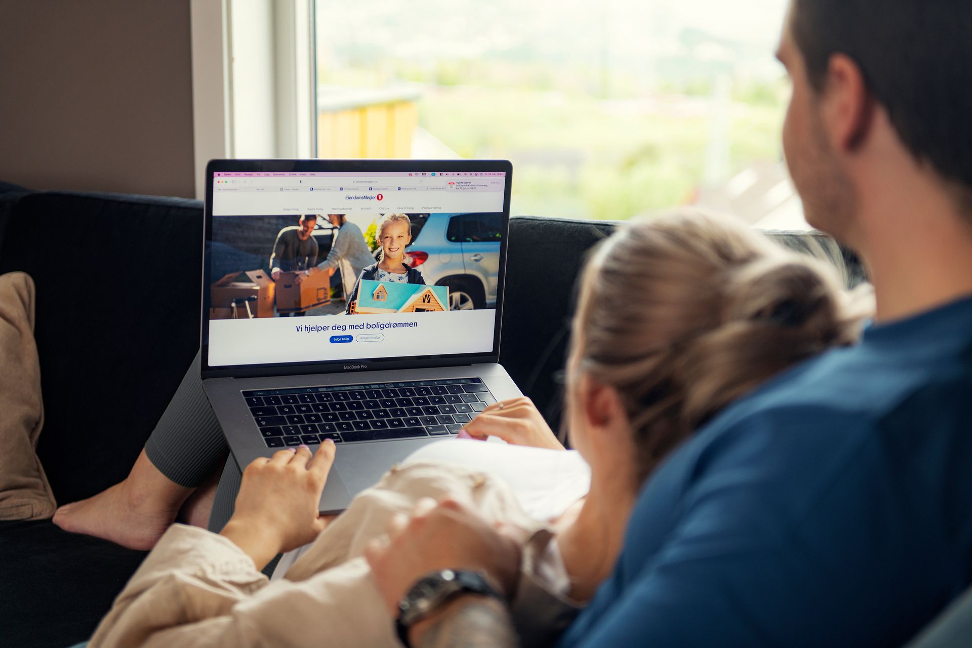Foto av kvinne og mann som sitter tett sammen i en sofa ser på en mac-skjerm. 
