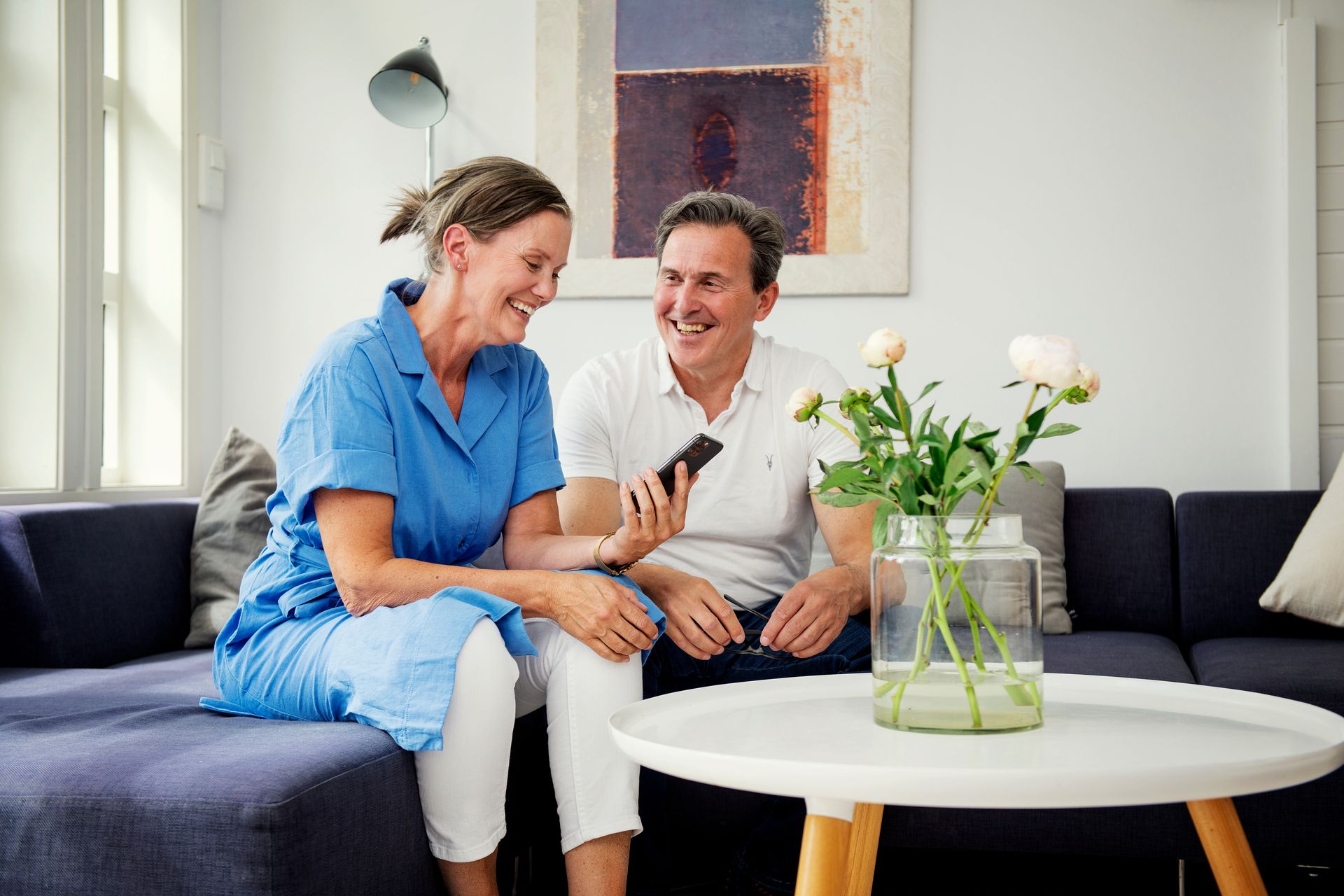 Par sitter i sofa, smiler og ser på en telefon. Foto
