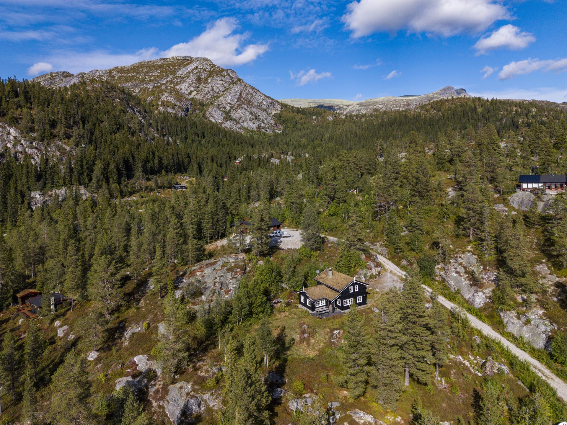 Eiendommen ligger skjermet til i skrånende terreng omgitt av furuskog og fjellformasjoner.. Bilde nummer 3 av 3