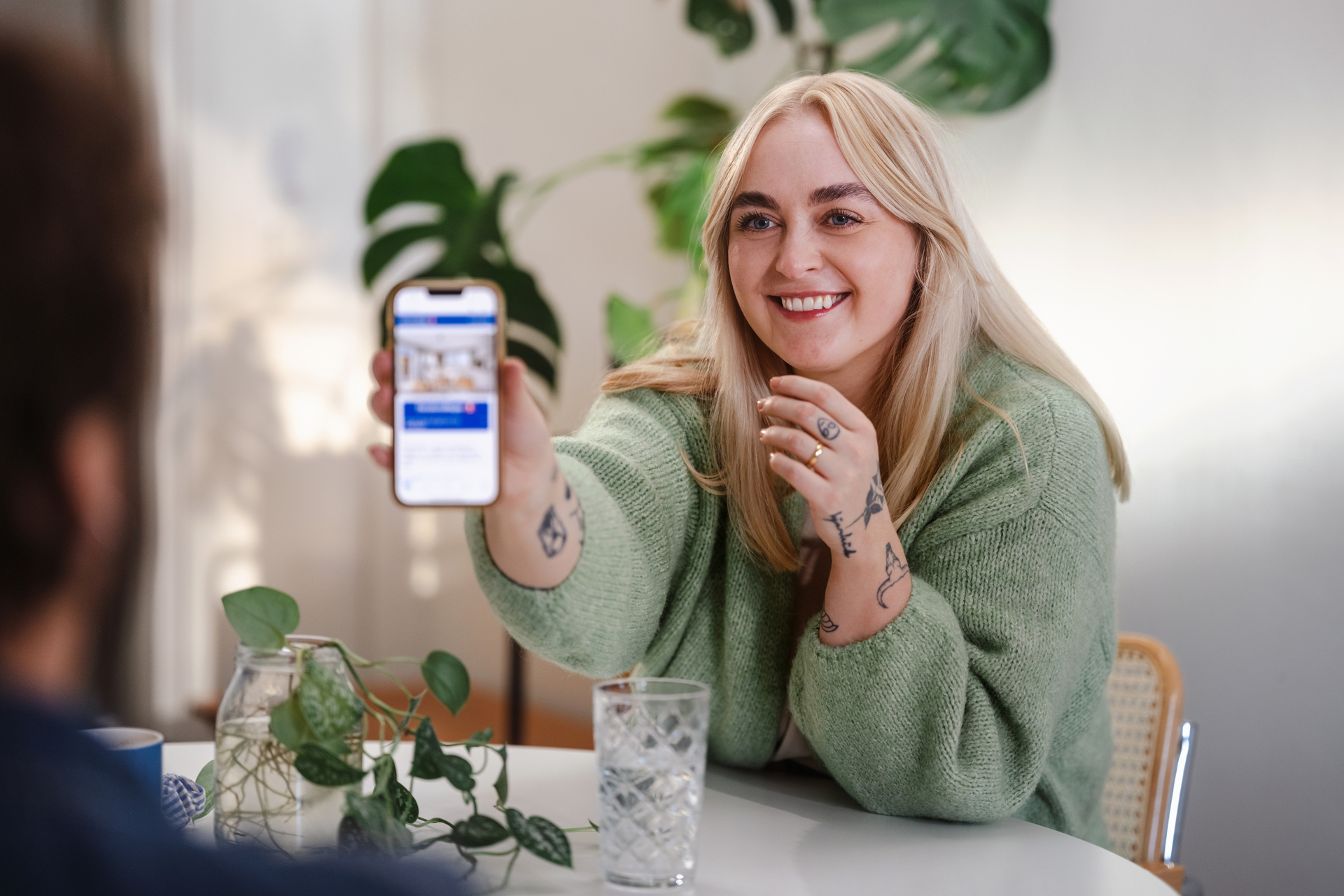 Foto av ung kvinne som viser en boligannonse på telefonen til en mann som sitter i forgrunnen.