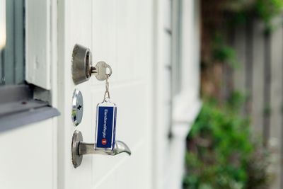 Nøkkel står i låsen på en hvit dør. Blå nøkkelring med EiendomsMegler 1-logo. Foto