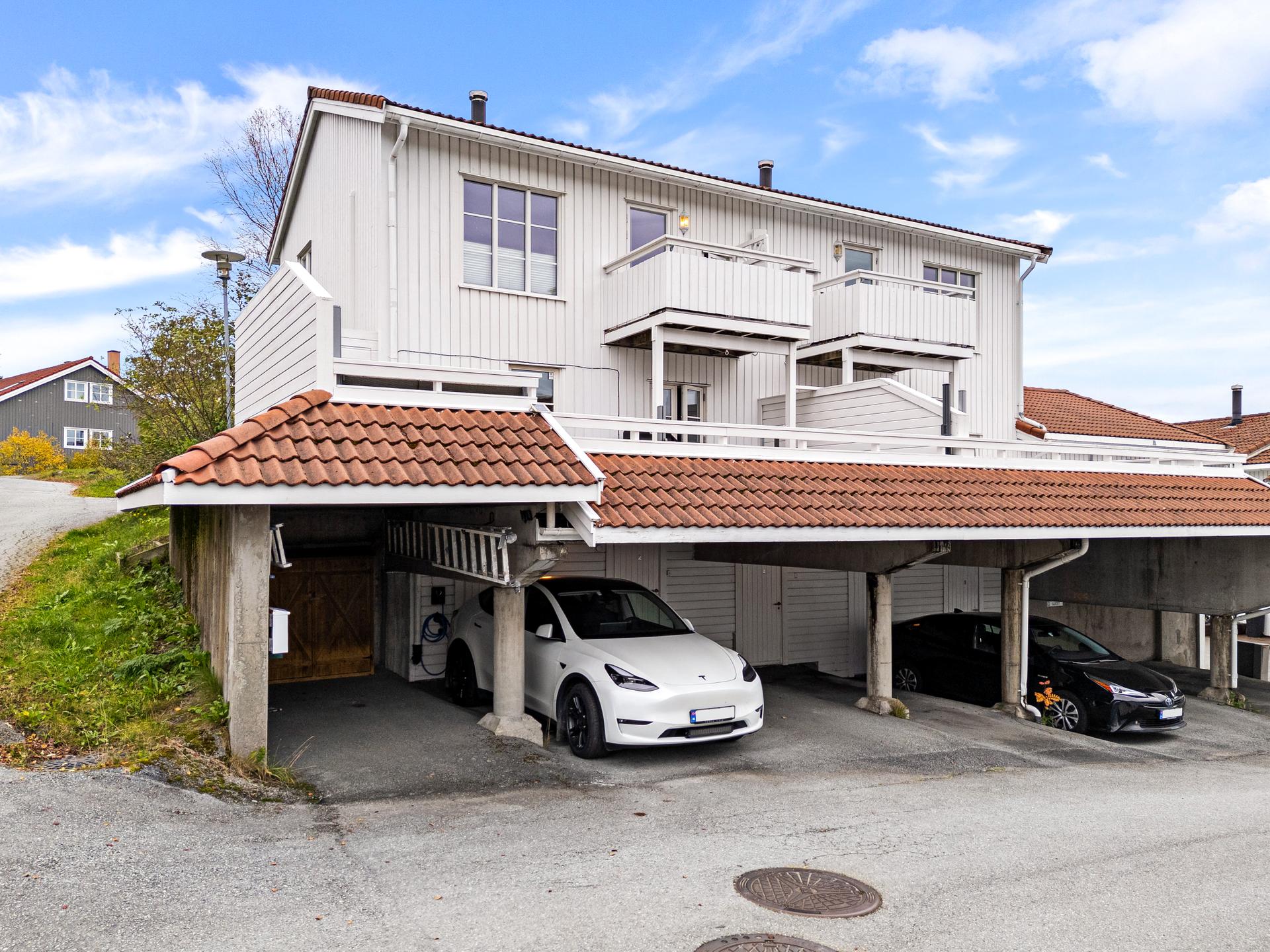Carport med asfaltert dekke, elbillader installert i 2023 og praktisk utebod i bakkant. Bilde nummer 2 av 3
