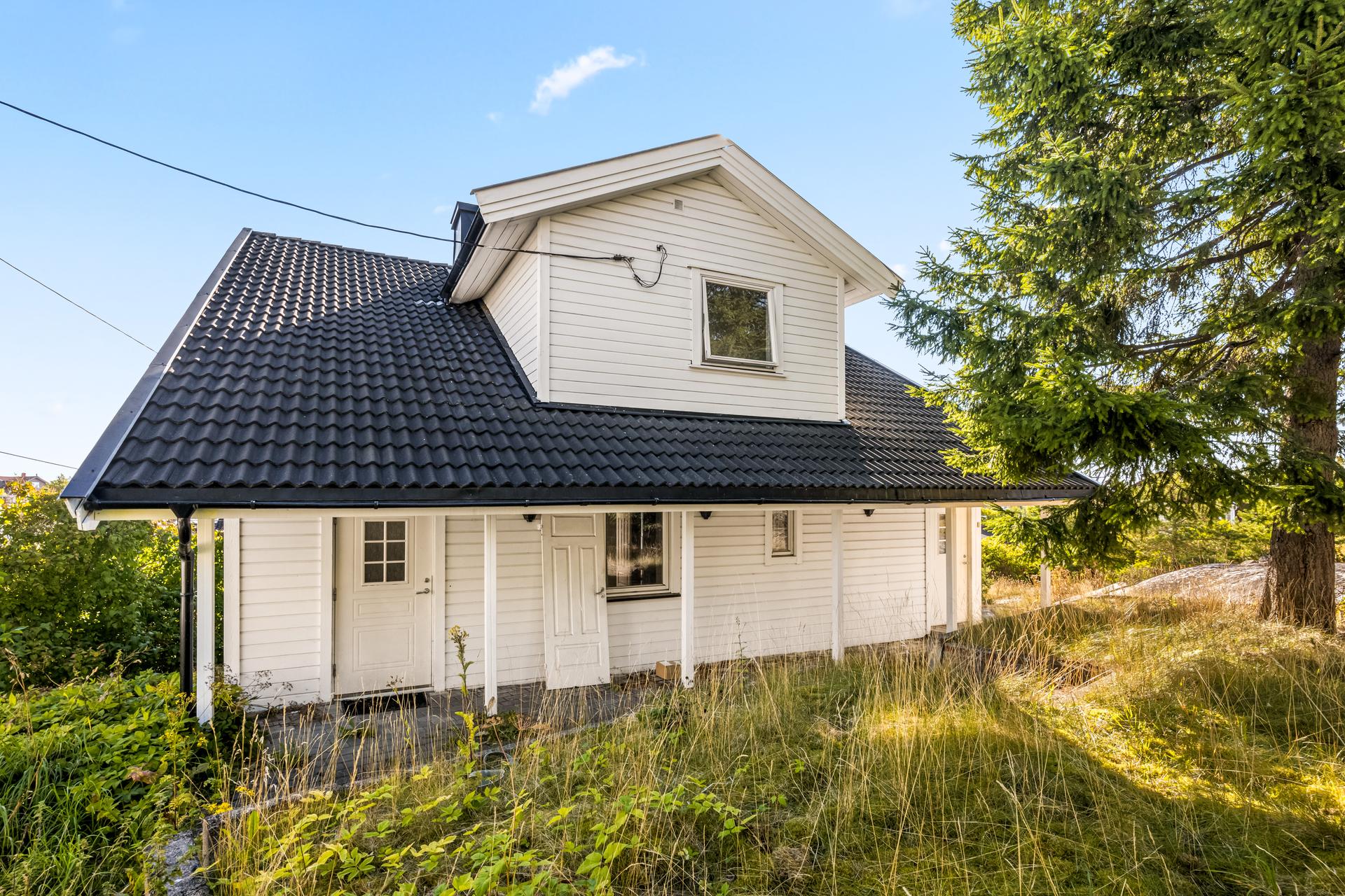 Huset har hvitmalt kledning og tak tekket med betongtakstein, omkranset av hage og naturtomt.. Bilde nummer 2 av 3