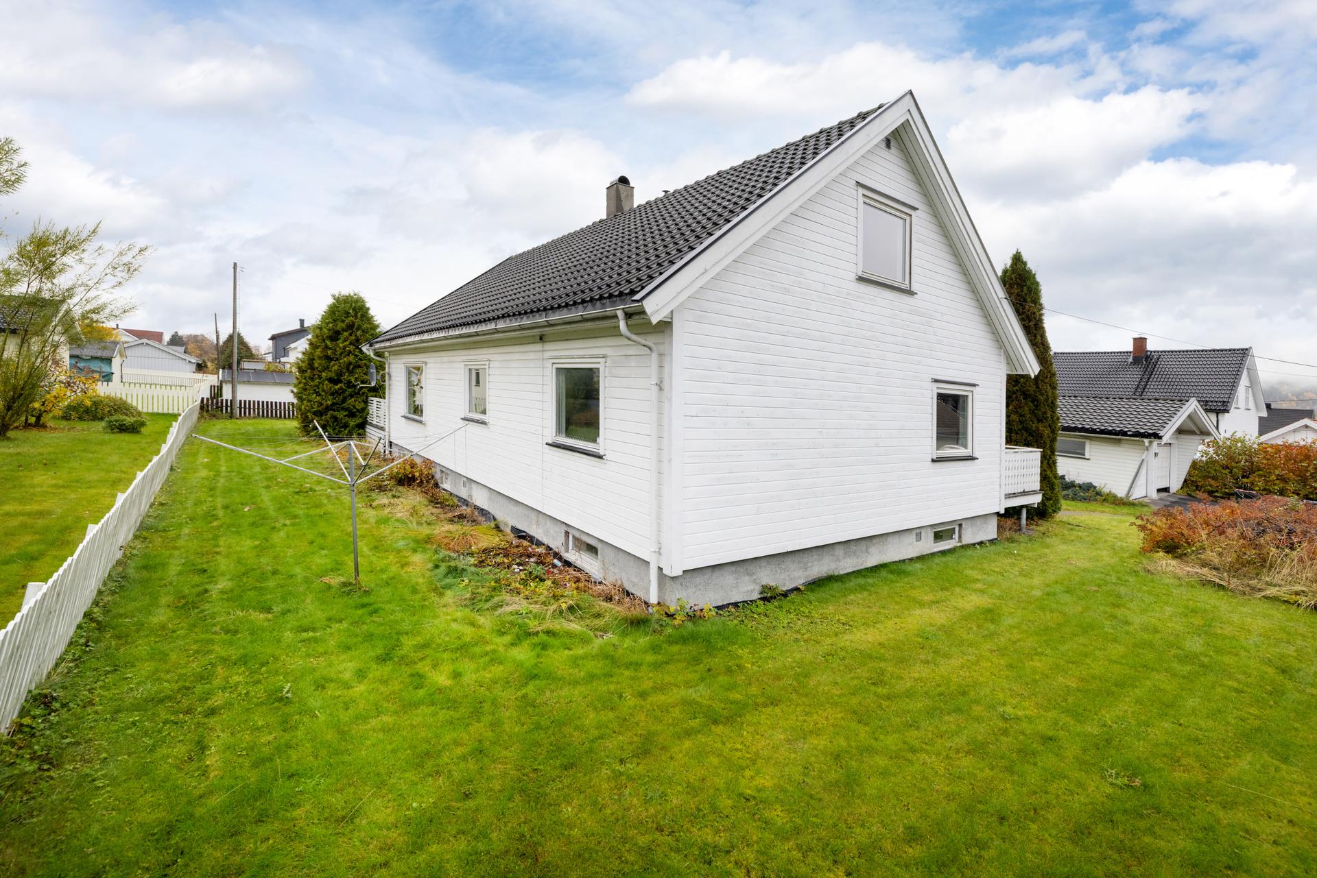 Eiendommen har en flat og opparbeidet tomt med stor gressplen og hekkbeplantning.. Bilde nummer 3 av 3