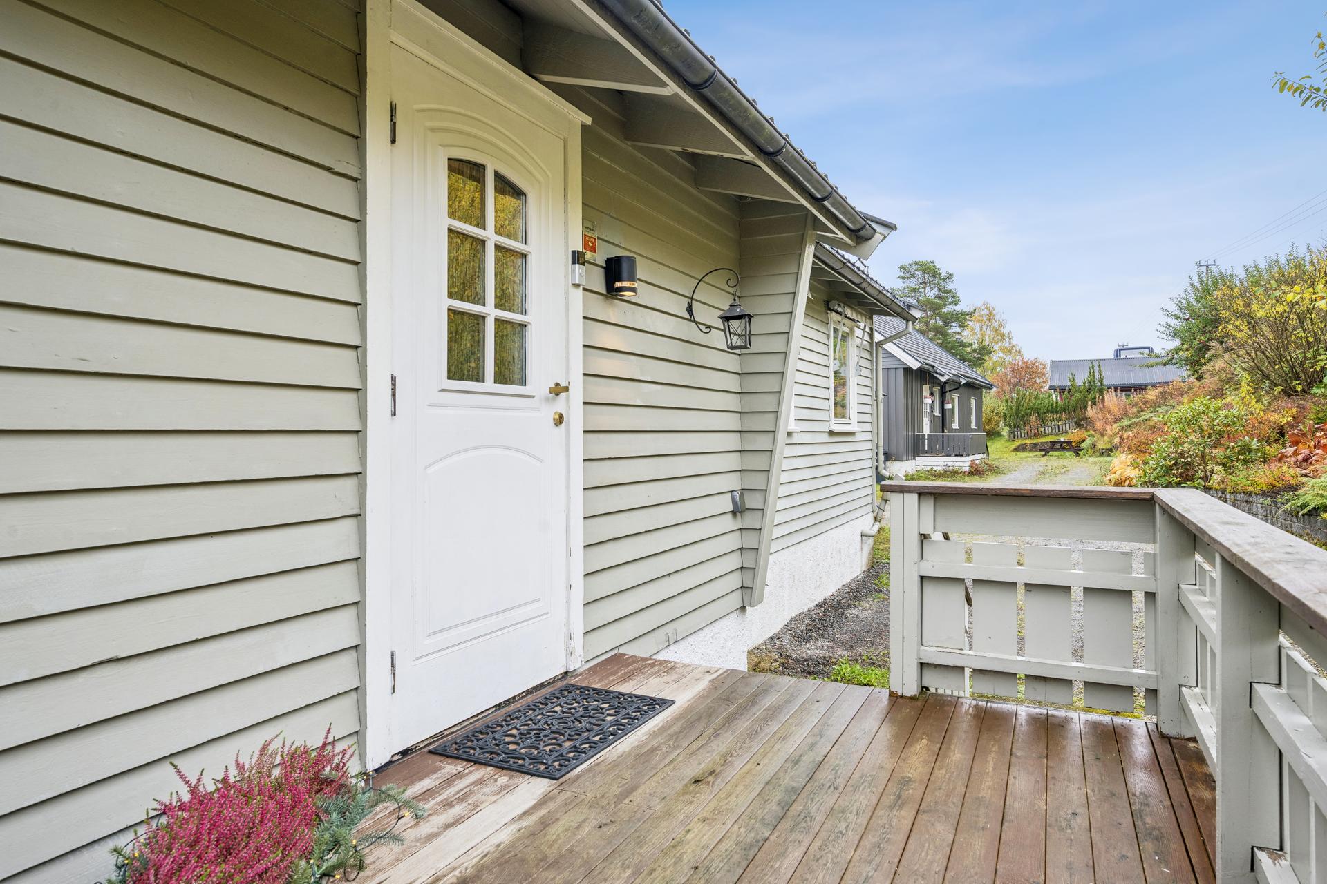 Overbygd inngangsparti med terrasse i treverk og trappeadkomst fra gårdsplassen.. Bilde nummer 3 av 3