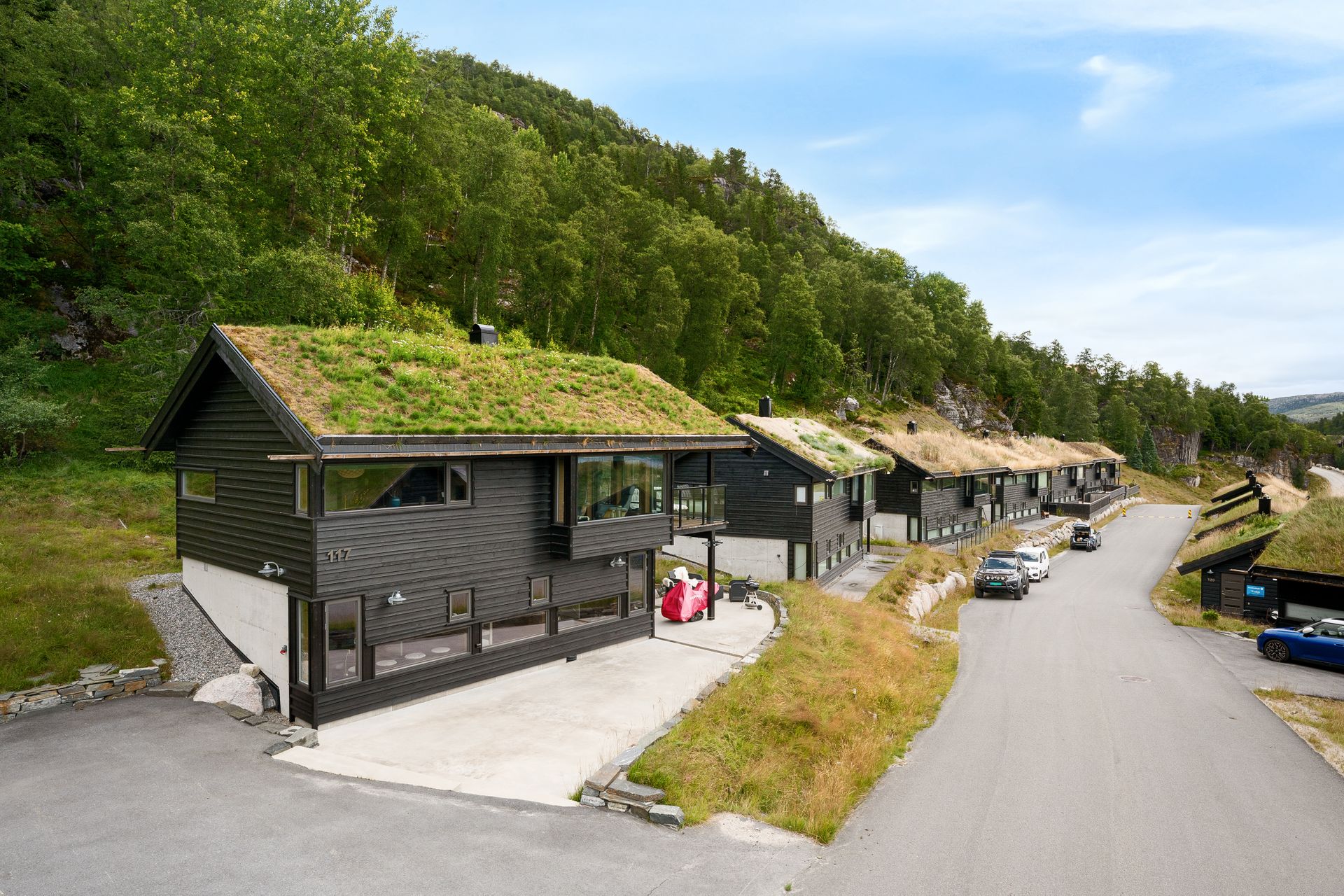 God parkering ved hytten på egen plass med ladepunkt på hytteveggen. Store, helstøpte uterom i front og på siden - for enkelt vedlikehold og snørydding. Her kan du møblere i flere soner og ha grill/bålpanne. . Bilde nummer 2 av 3
