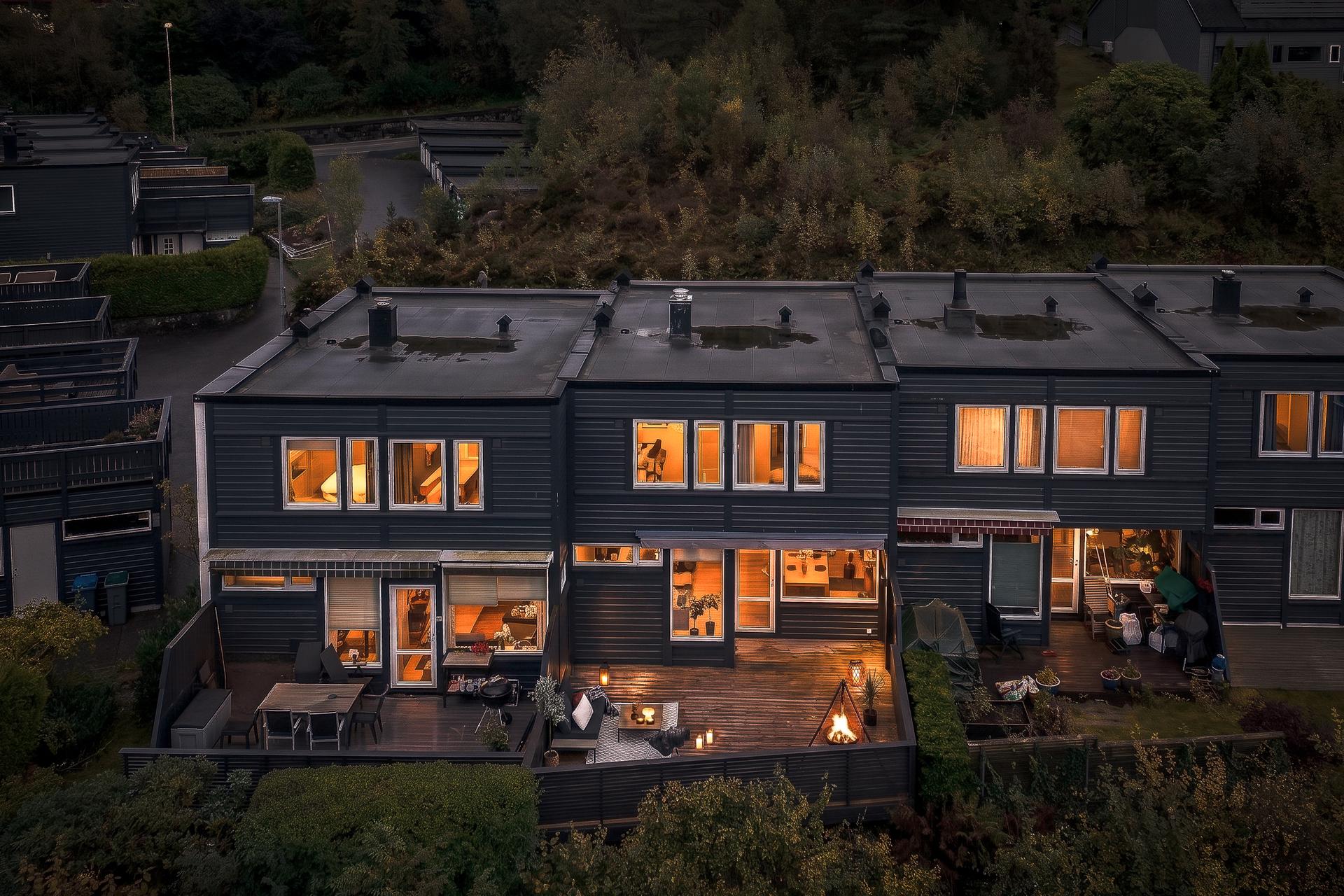 Rekkehuset opplyst på kveldstid med terrassen i forkant.. Bilde nummer 2 av 3