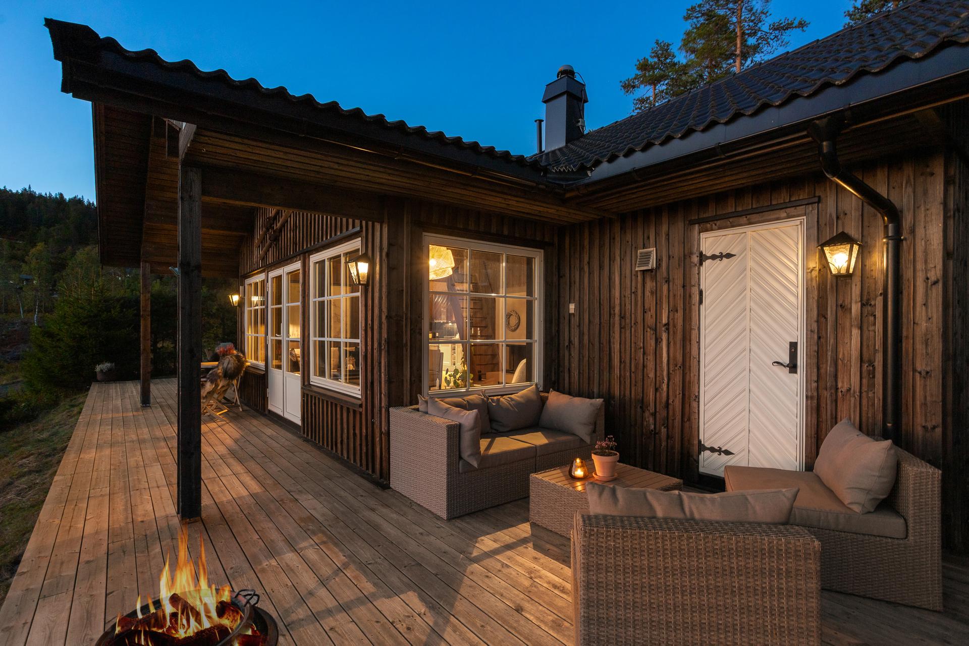 Overbygd del av verandaen med utelamper og lun sitteplass inntil hytteveggen. Den hvite døren fører inn til badstuen og videre inn i hytta.. Bilde nummer 2 av 3