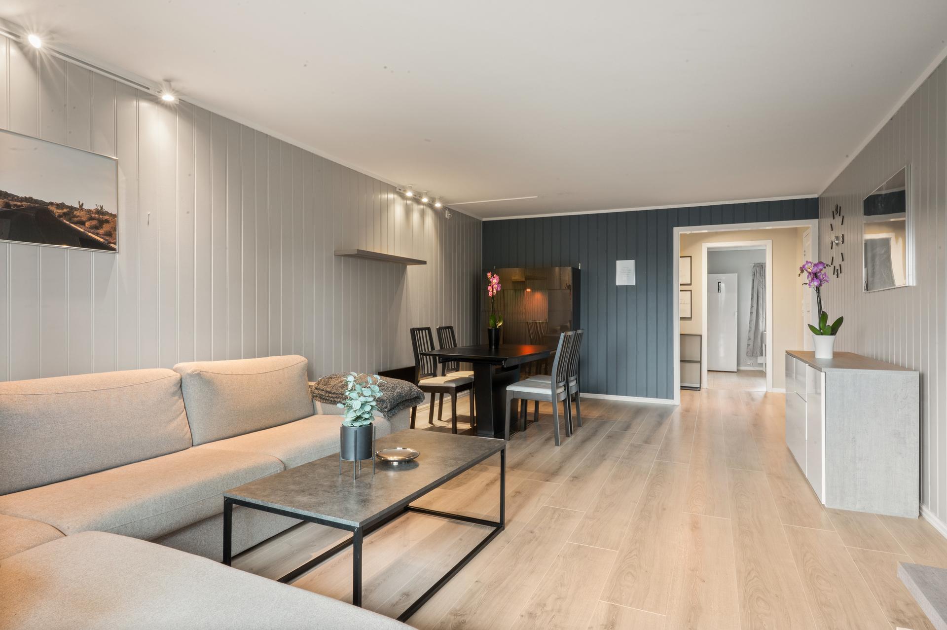 Stuen har god plass til både sofagruppe og spisebord, med slettmalte flater og malt panel på veggene.. Bilde nummer 2 av 3