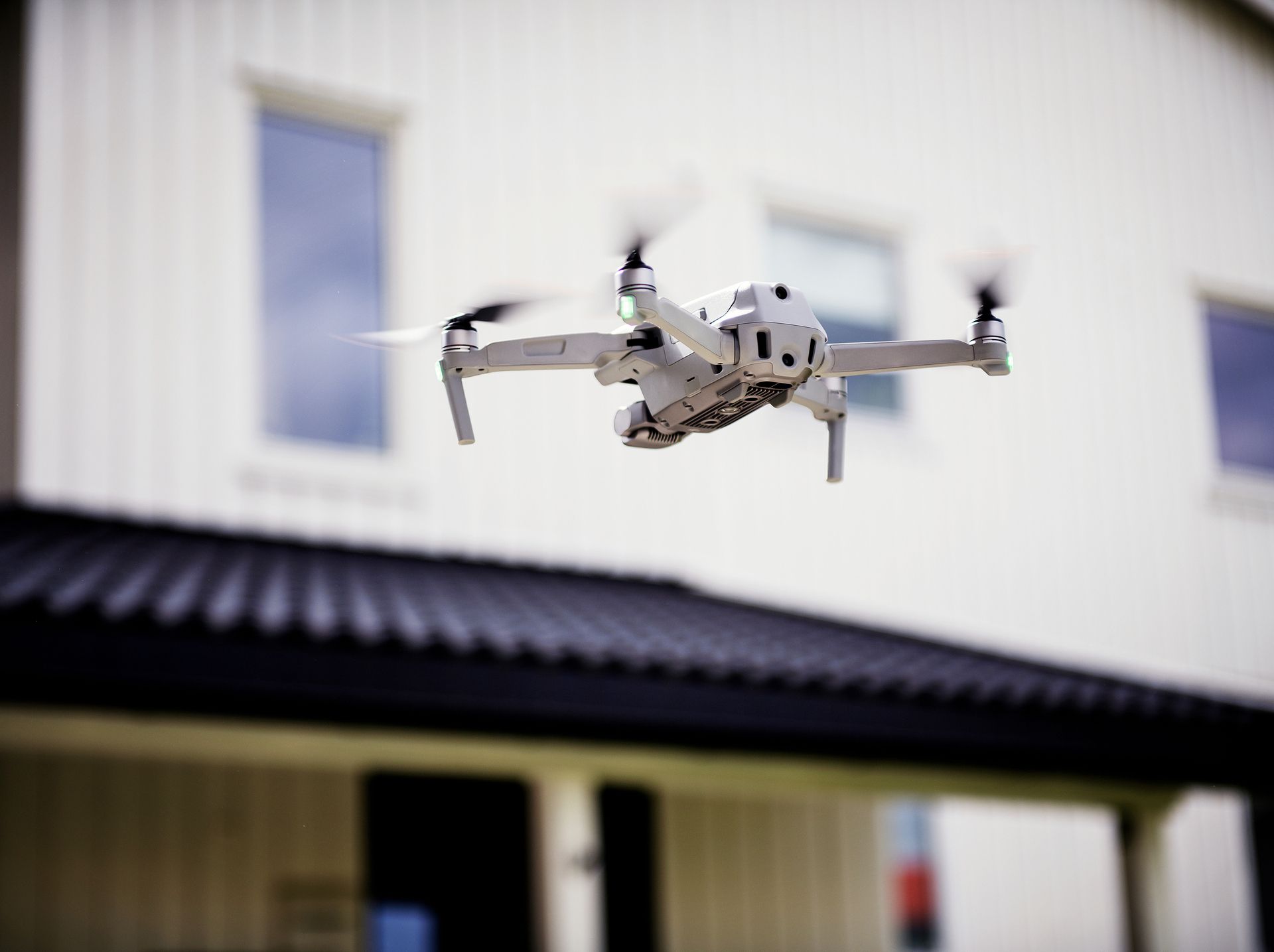 Nærbilde av drone som flyr foran hvitt hus. Foto.

