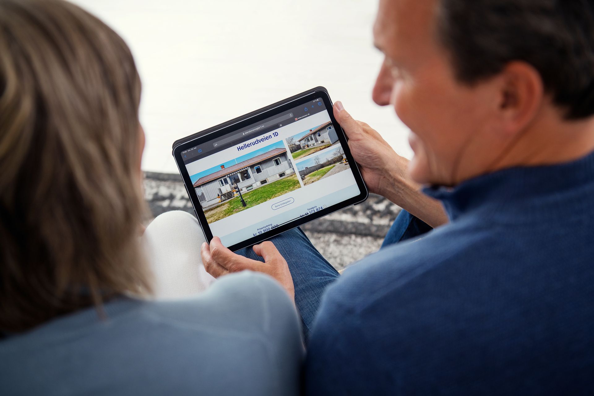 Par sitter med ryggen til kamera og ser på en eiendom på en tablet. Foto.
