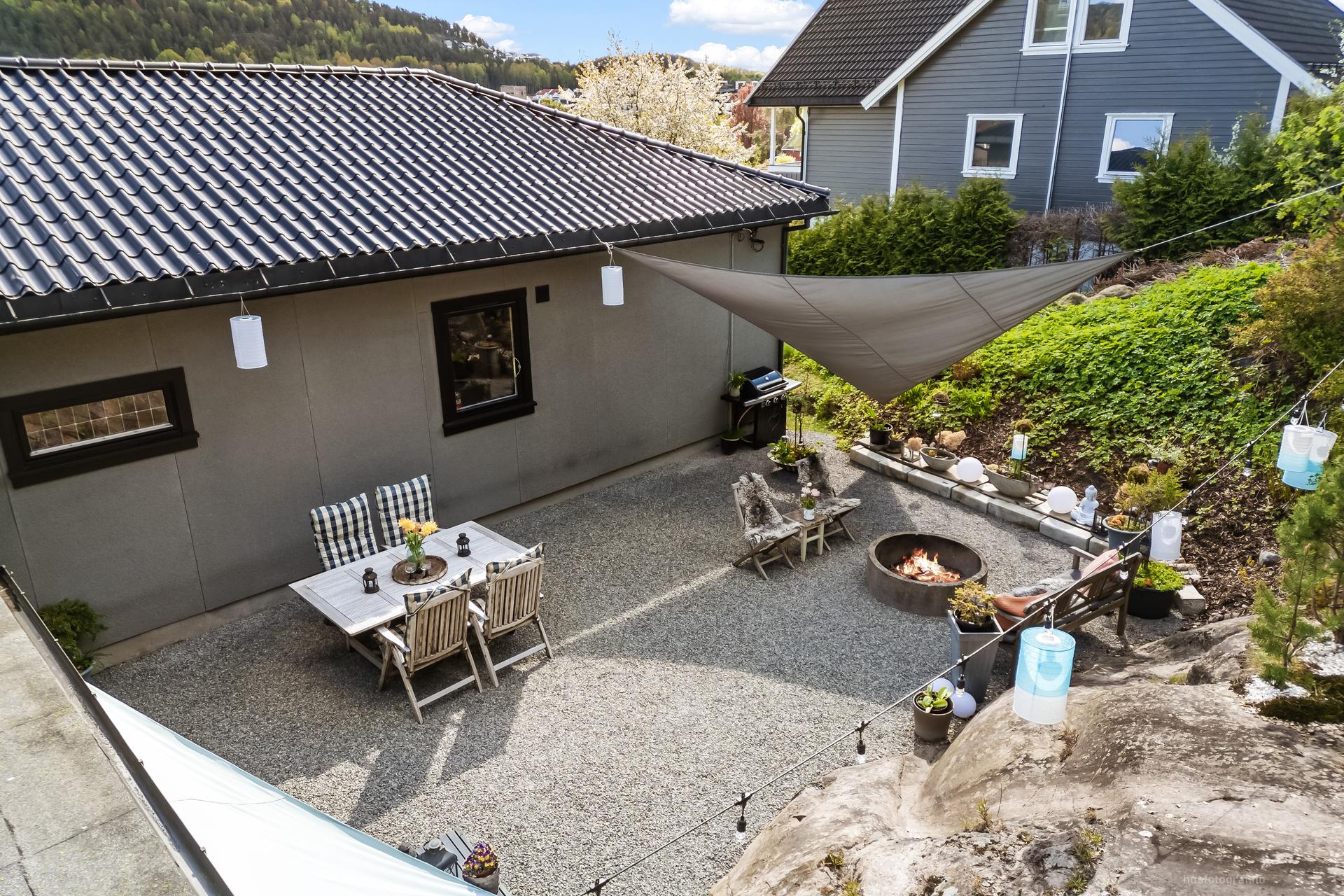 Tomten er opparbeidet med en lettstelt, gruset uteplass og ligger i et skrånende terreng med skogen som nærmeste nabo.. Bilde nummer 3 av 3