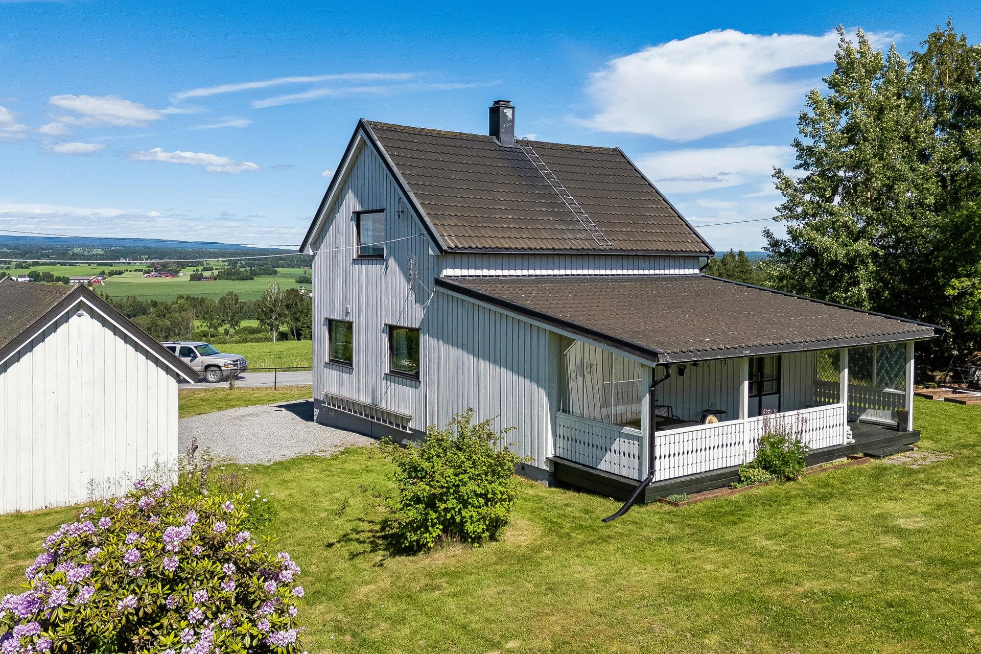 Eiendommen ligger på en hellende tomt med hage og plen.. Bilde nummer 2 av 3