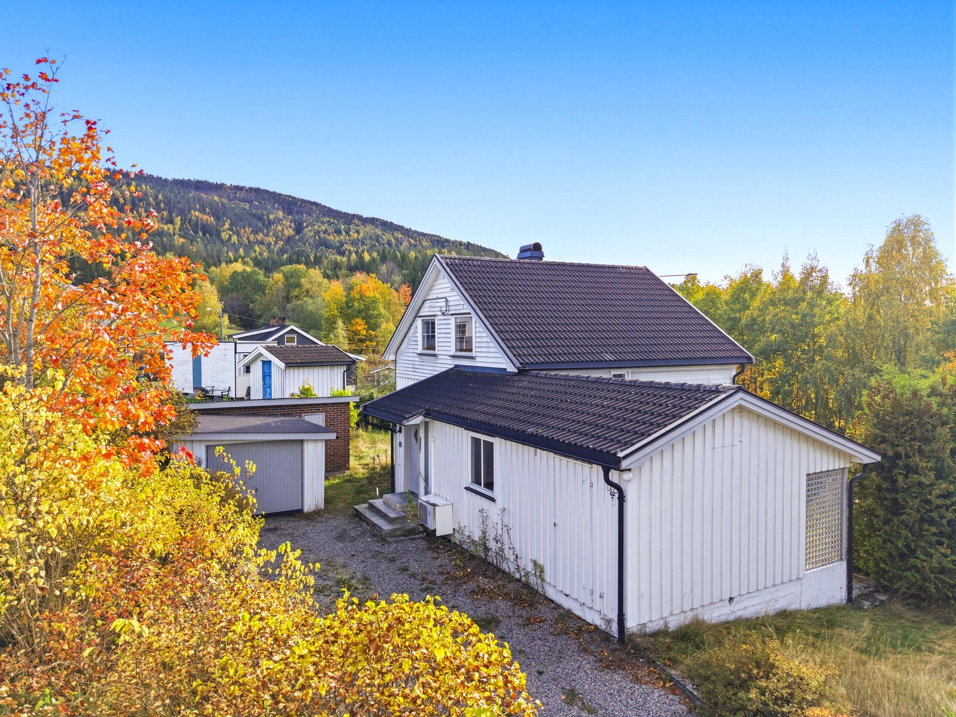 Eiendommen har romslig tomt med frittstående garasje og skogkledde åser i bakgrunnen.. Bilde nummer 3 av 3