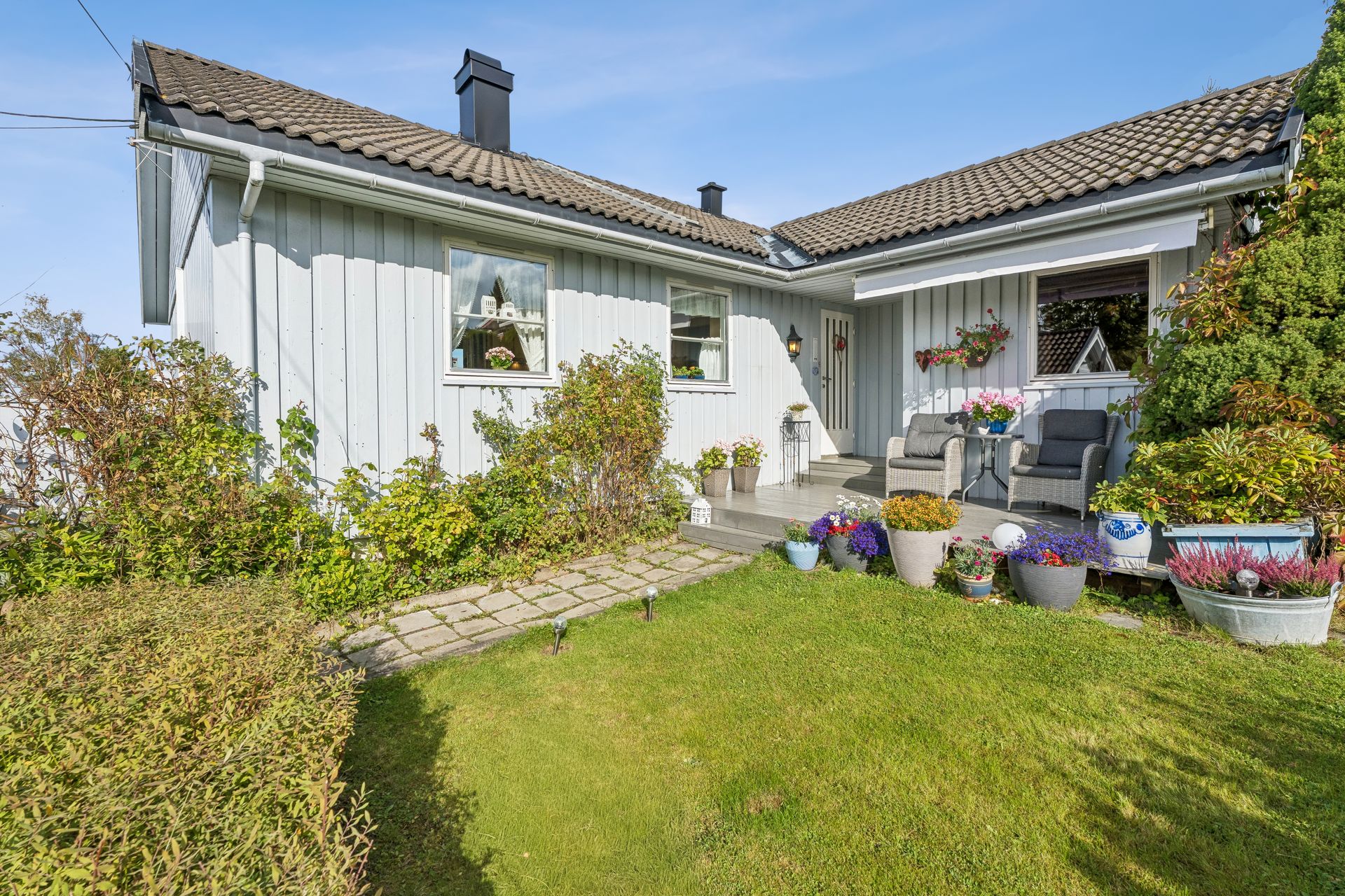 Inngangspartiet har hellelagt gangvei, frodig beplantning og en lun sitteplass.. Bilde nummer 3 av 3
