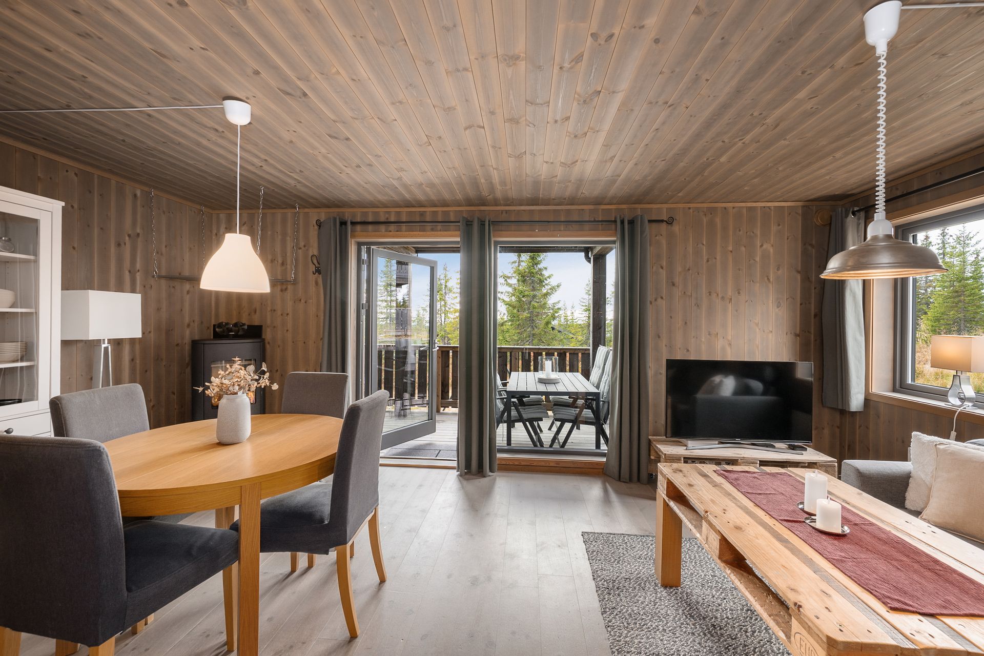 Stue og kjøkken i åpen løsning med peisovn og utgang til overbygd terrasse.. Bilde nummer 3 av 3