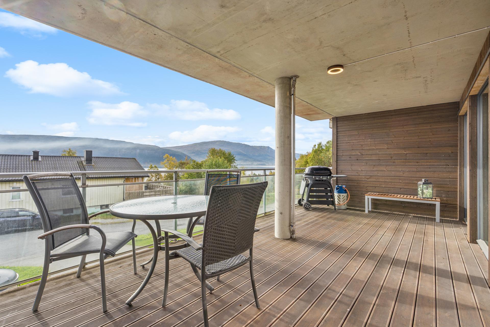 Overbygd balkong med terrassedekke av tre, glassrekkverk og utsikt mot Ranfjorden.. Bilde nummer 3 av 3