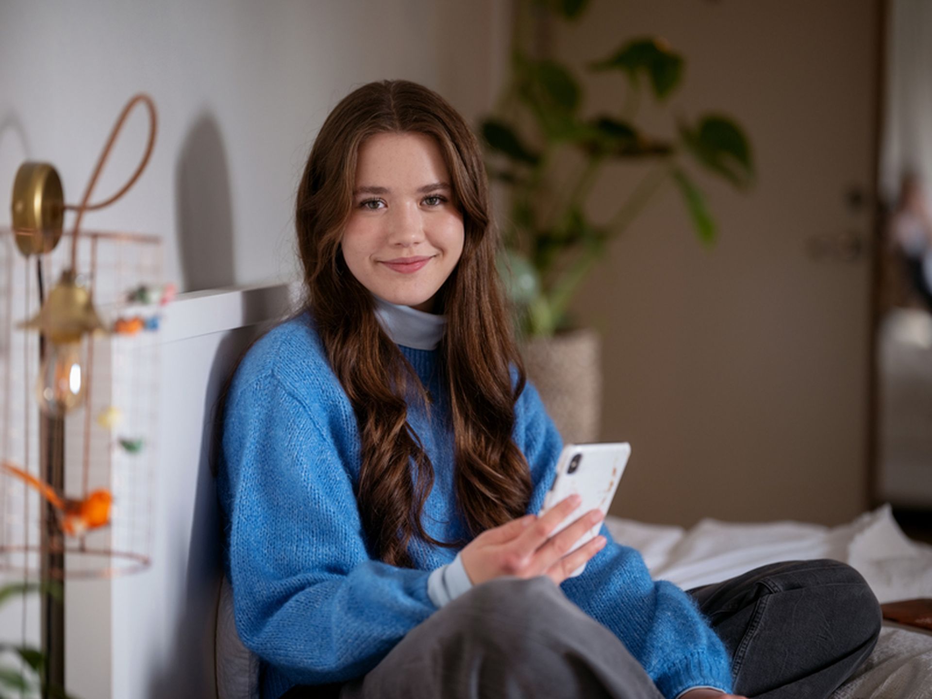 Student holder mobiltelefon mens hun sitter i sengen