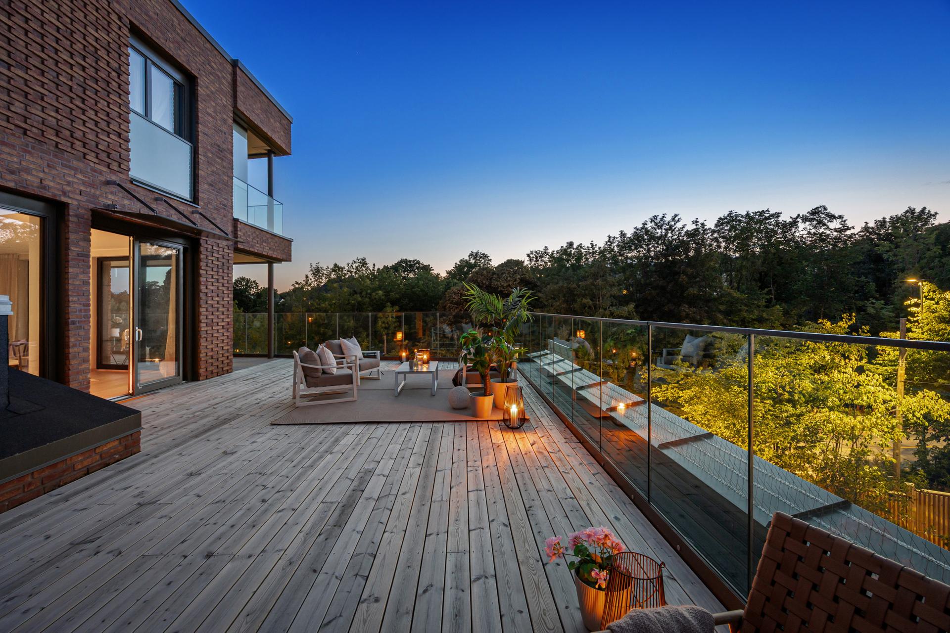 Hele terrassen har dekke av terrassebord, rekkverk i glass og diskret vegglamper i sort design.. Bilde nummer 2 av 3