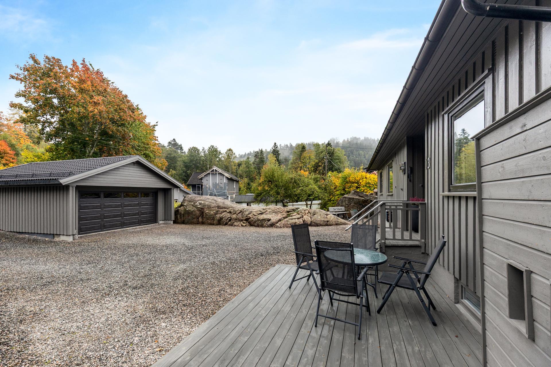 Plattingen ved inngangspartiet vender ut mot den gruslagte gårdsplassen med stor garasje.. Bilde nummer 3 av 3