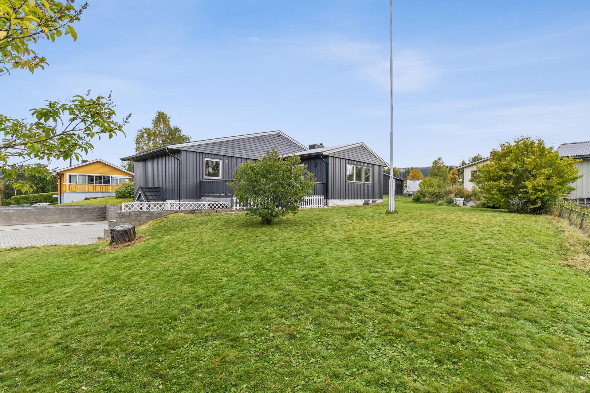 Tomten er opparbeidet med en stor, flat gressplen og beplantning.. Bilde nummer 2 av 3