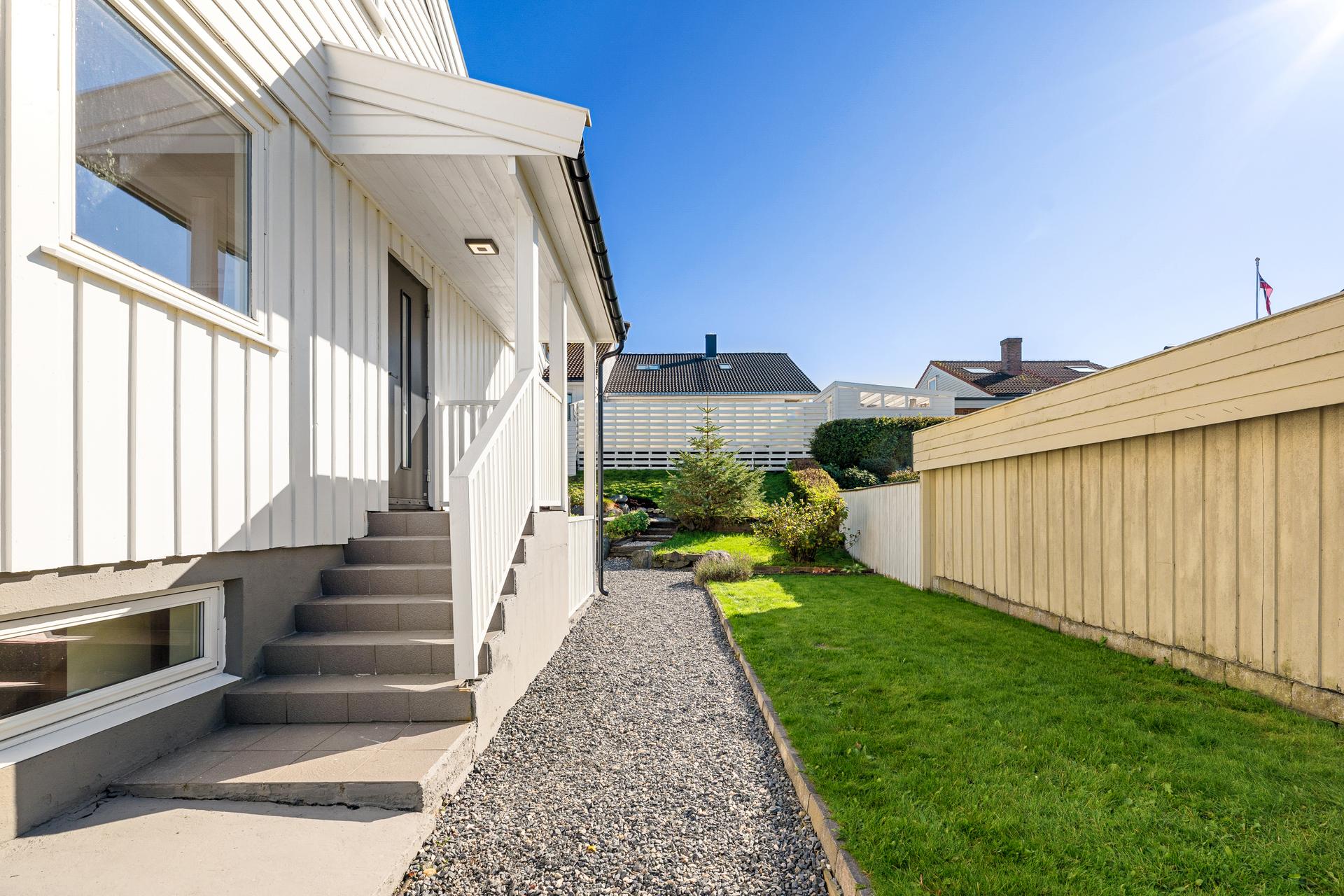Gruset gangsti langs husveggen leder inn til inngangspartiet og hagen.. Bilde nummer 3 av 3