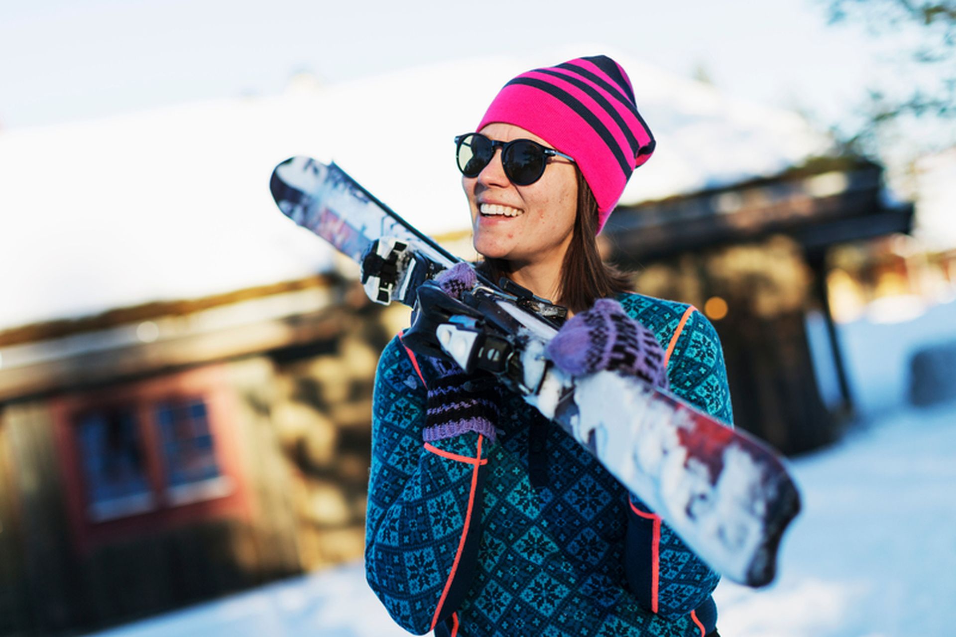 Slalomski på fjellet med snø og hytte i bakgrunnen - kvinne holder dem med rosa lue