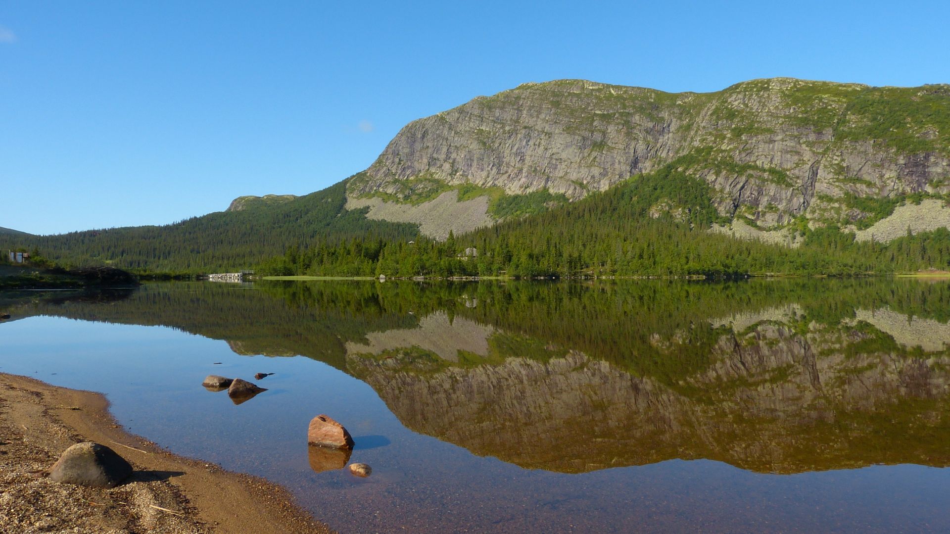 Fjellvann hvor fjellet speiler seg i vannet med skyfri himmel